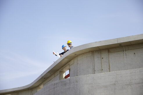 Two men on construction site discussing construction plan - FMKF001586