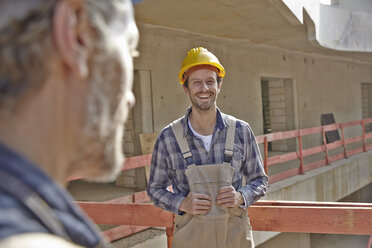Smiling man with hard hat on construction site - FMKF001591