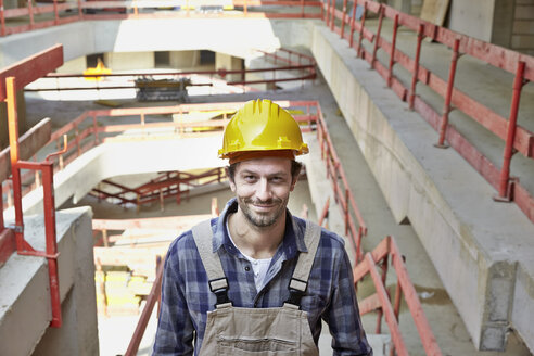 Smiling man with hard hat on construction site - FMKF001596