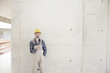 Mann mit Schutzhelm auf einer Baustelle an einer Betonwand - FMKF001601