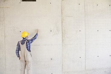 Mann mit Schutzhelm auf einer Baustelle, der auf eine Betonwand zeichnet - FMKF001602