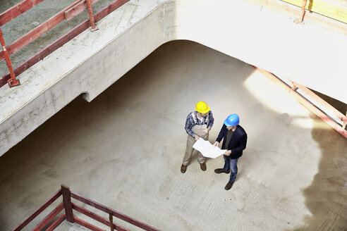 Construction worker and architect with plan talking on construction site - FMKF001605