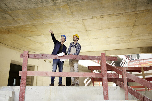 Construction worker and architect talking on construction site - FMKF001607