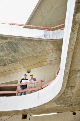Bauarbeiter und Architekt mit Plan im Gespräch auf der Baustelle, lizenzfreies Stockfoto