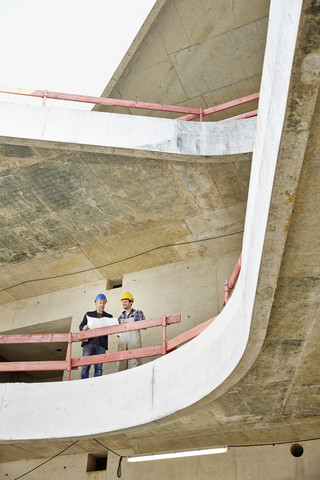 Construction worker and architect with plan talking on construction site stock photo