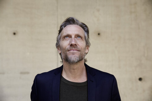 Portrait of confident mature man at concrete wall looking up - FMKF001613