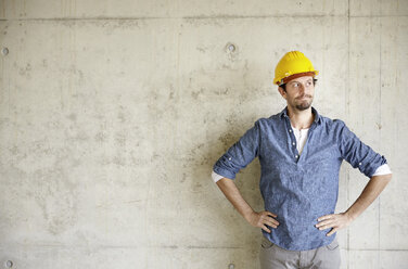 Mann mit Schutzhelm an Betonwand denkt nach - FMKF001628