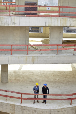 Zwei Männer mit Schutzhelmen unterhalten sich auf einer Baustelle, lizenzfreies Stockfoto