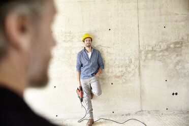Man with hard hat site standing at concrete wall holding drill - FMKF001633