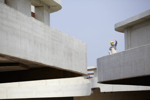 Man on construction site raising his hand - FMKF001635