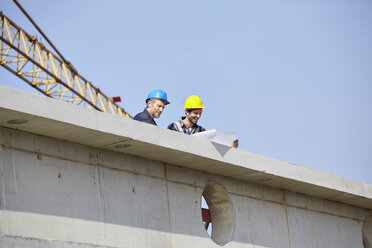 Zwei Männer auf einer Baustelle mit Blick auf einen Bauplan - FMKF001725