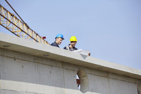 Two men on construction site looking at construction plan - FMKF001725