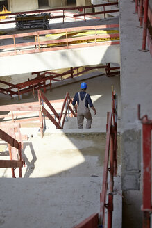 Man with hard hat on construction site walking downstairs - FMKF001727