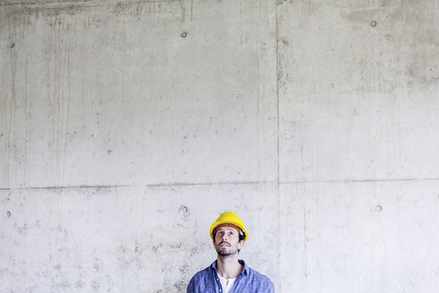 Man with hard hat on construction site at concrete wall looking up - FMKF001660