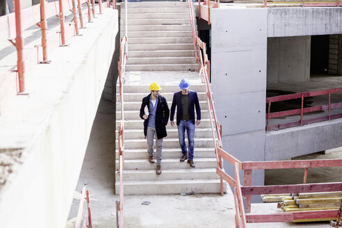 Two men on construction site walking down stairs - FMKF001661