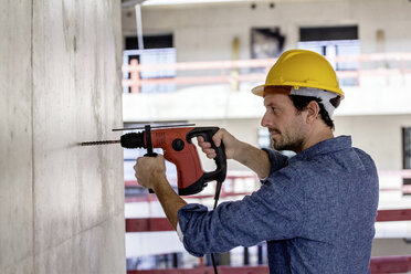 Mann mit Schutzhelm auf einer Baustelle mit Bohrmaschine - FMKF001663