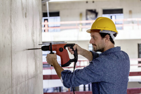 Man with hard hat on construction site using drill - FMKF001663