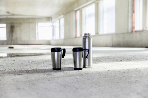 Thermos flask and mugs on concrete floor on construction site - FMKF001672