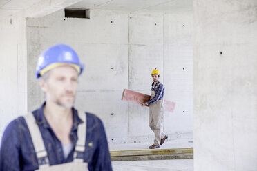 Arbeiter auf einer Baustelle trägt ein Holzbrett - FMKF001676