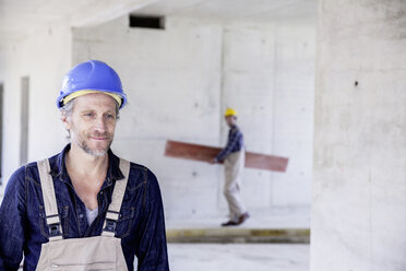 Smiling worker on construction site with colleague in background - FMKF001677