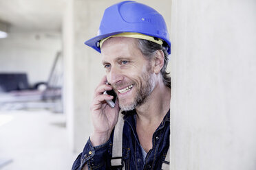 Smiling worker on construction site on cell phone - FMKF001679