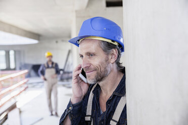 Lächelnder Arbeiter auf einer Baustelle mit Handy - FMKF001680