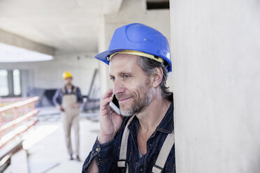 Smiling worker on construction site on cell phone - FMKF001680