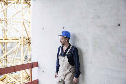 Worker on construction site standing at concrete wall - FMKF001681