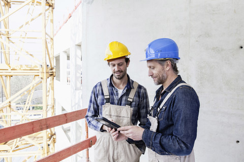 Zwei Bauarbeiter auf einer Baustelle mit Blick auf ein digitales Tablet, lizenzfreies Stockfoto
