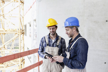 Two construction workers on construction site looking at digital tablet - FMKF001732