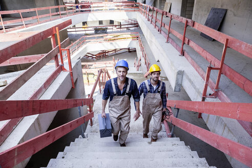Two construction workers on construction site walking upstairs - FMKF001684