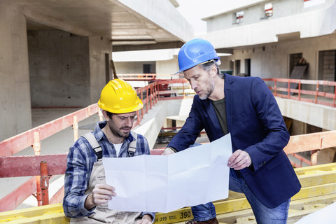 Construction worker and architect with plan talking on construction site stock photo