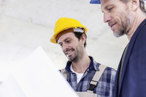 Construction worker and architect with plan talking on construction site stock photo