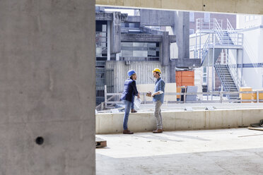 Zwei Männer mit Schutzhelmen unterhalten sich auf einer Baustelle - FMKF001691