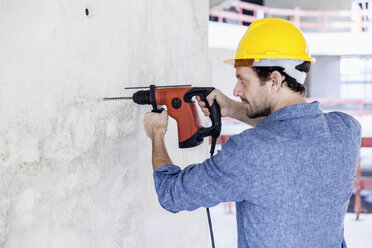 Mann mit Schutzhelm auf einer Baustelle mit Bohrmaschine - FMKF001694