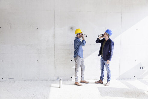 Zwei Männer auf einer Baustelle trinken aus Bechern - FMKF001697