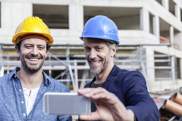 Two happy men on construction site taking a selfie - FMKF001700