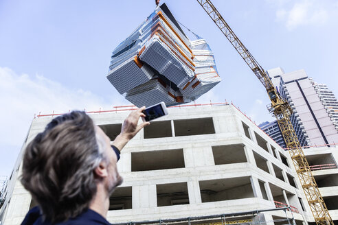 Man taking picture of loaded crane on construction site - FMKF001701