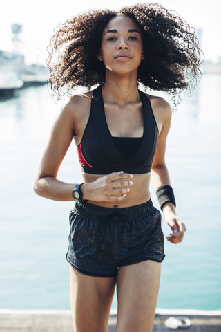 Spanien, Barcelona, Porträt einer joggenden jungen Frau vor dem Hafen, lizenzfreies Stockfoto