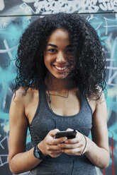 Portrait of smiling young woman hearing music with earphones - EBSF000751