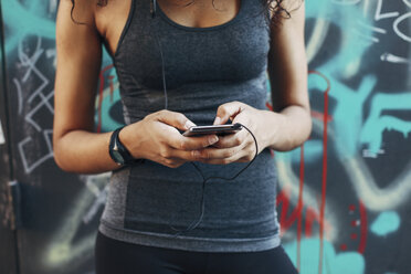 Young woman holding smartphone hearing music with earphones, close-up - EBSF000753