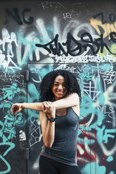 Porträt einer lächelnden jungen Frau, die vor einer Graffiti-Wand steht - EBSF000754