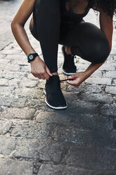 Sportive young woman tying her shoe on pavement - EBSF000757