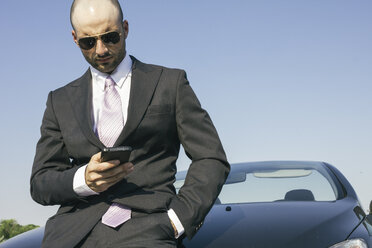 Businessman with sunglasses leaning against car looking on cell phone - ABZF000202