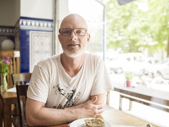 Deutschland, Berlin, Älterer Mann sitzt im Café und schaut in die Kamera - TAM000224