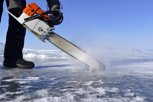 Russland, Baikalsee, Mann öffnet ein Eisloch mit einer Motorsäge zum Eistauchen - GNF001337