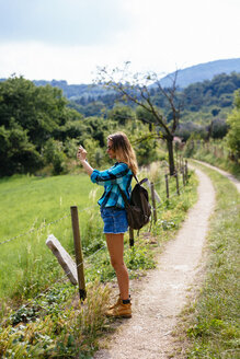 Südtirol, junges Mädchen mit Rucksack, das auf einem Weg steht und ein Foto macht - GIOF000064