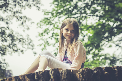 Porträt eines kleinen Mädchens, das auf einem großen Baumstamm sitzt, lizenzfreies Stockfoto