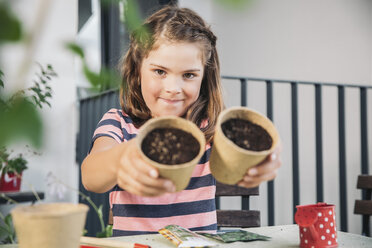 Little girl showing flowerpots with seeds and soil on the balcony - MFF001720