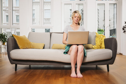 Frau sitzt auf einer Couch im Wohnzimmer und benutzt einen Laptop - MFF001747